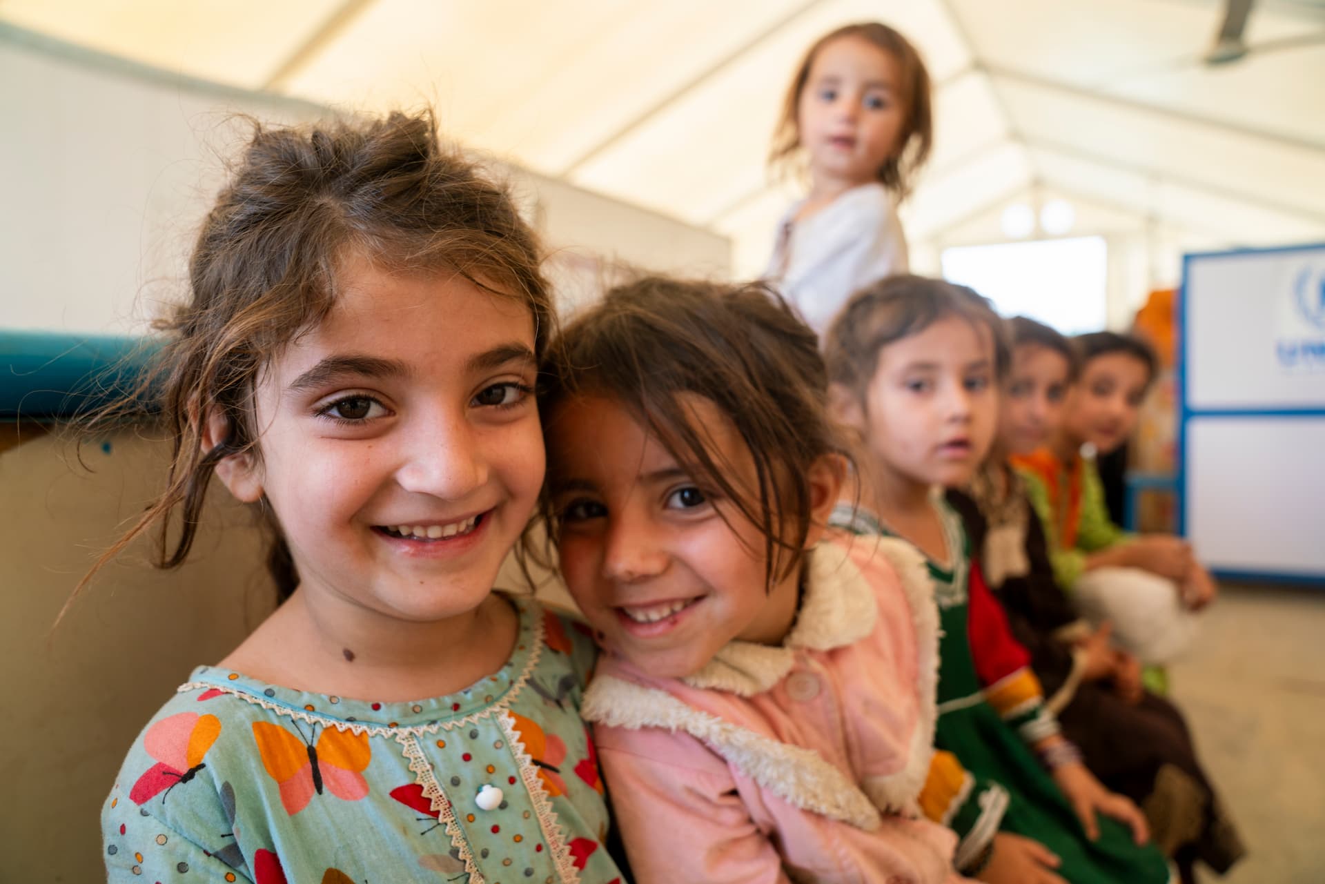Mahjabeen, 8, and her younger sister Negah, 5, recently returned from Pakistan. At the UNHCREncashment Center, they stay close to each other while their family receives cash assistance tohelp them begin a new chapter in Afghanistan. Amid the challenges, the sisters share a quietmoment of togetherness and hope. © UNHCR/Oxygen Empire Media Production